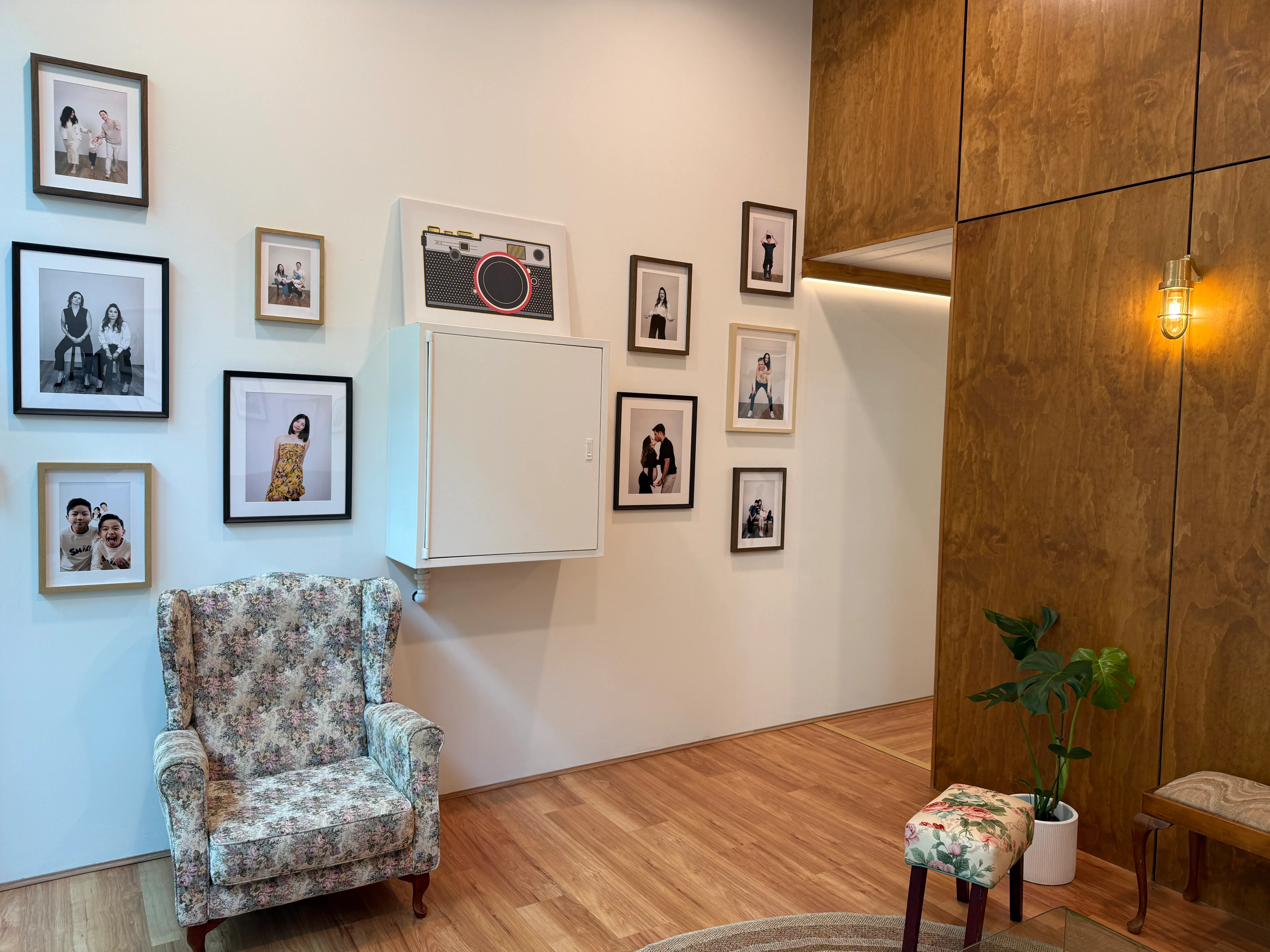 The Selforait Studio waiting area — a wall of framed client portraits beside a floral armchair, with timber panelling and a brass sconce